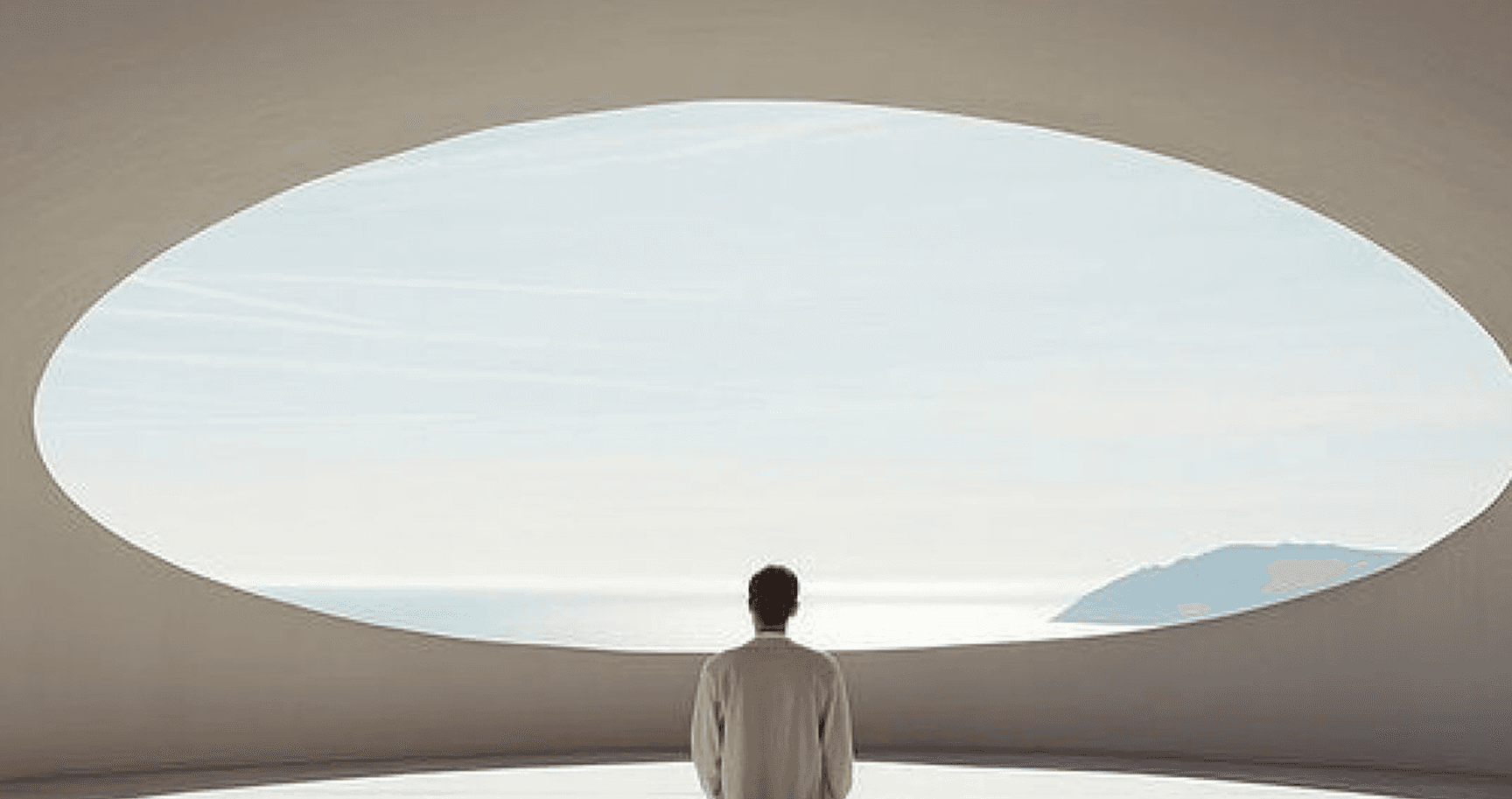 A person standing at a large oval window, looking out to the sea